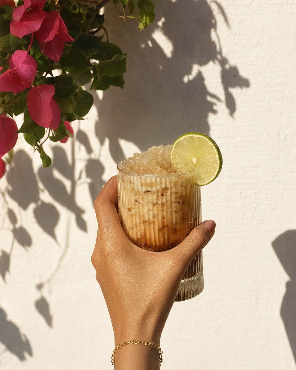 A hand holding a creamy soda against a sunlit plaster wall